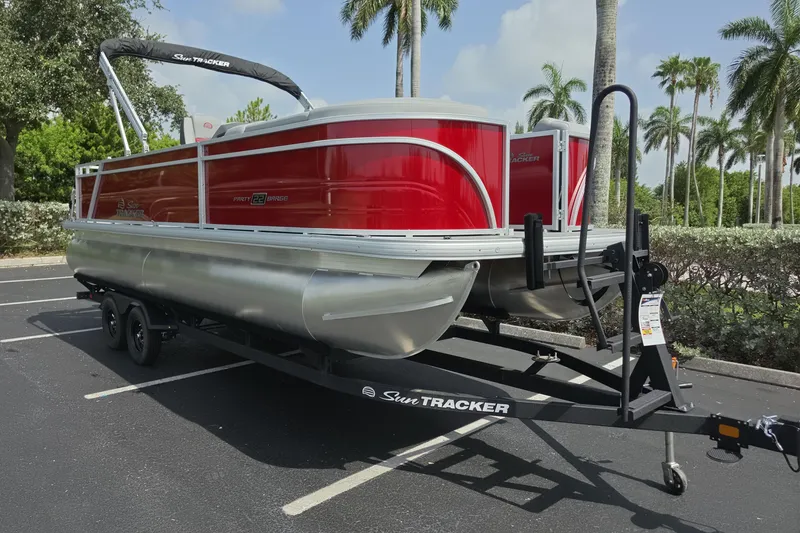 Slide: The Image of 2026 Sun Tracker Party Barge 22 RF DLX pontoon boat on trailer, parked under palm trees. - 4