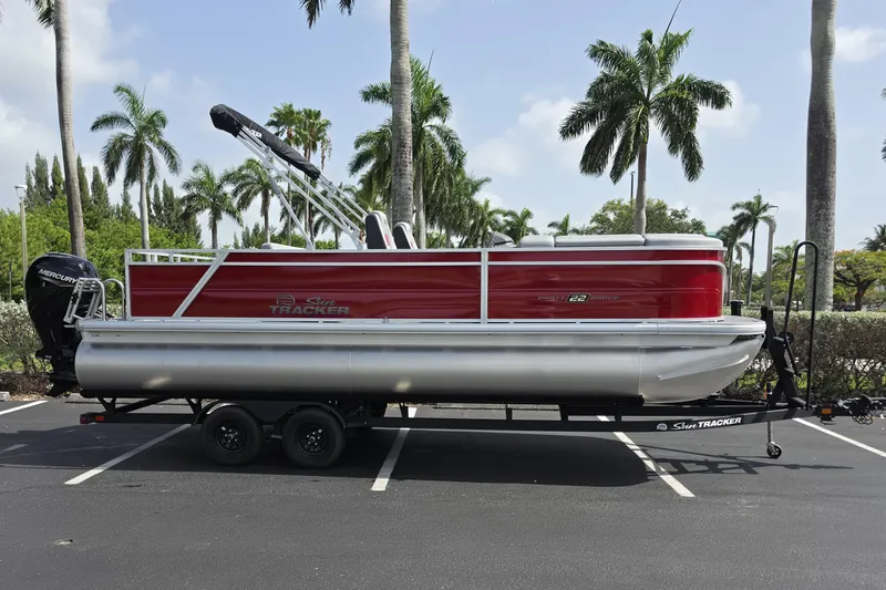 Slide: The Image of 2026 Sun Tracker Party Barge 22 RF DLX pontoon boat on trailer, parked with palm trees. - 1
