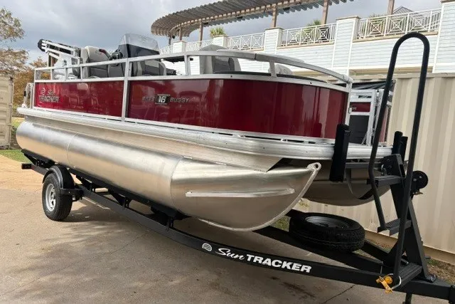Slide: The Image of 2026 Sun Tracker Bass Buggy 18 DLX pontoon boat on trailer, parked outdoors. - 14