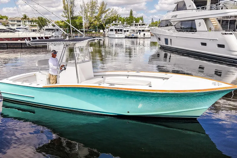 The Image of 1977 Scarborough 27 CC boat in marina, turquoise hull, man at helm, calm water. - 0