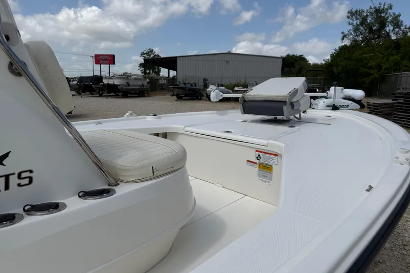 Slide: The Image of 2012 Mako 18 LTS boat interior with seating and storage, parked outdoors under cloudy sky. - 10