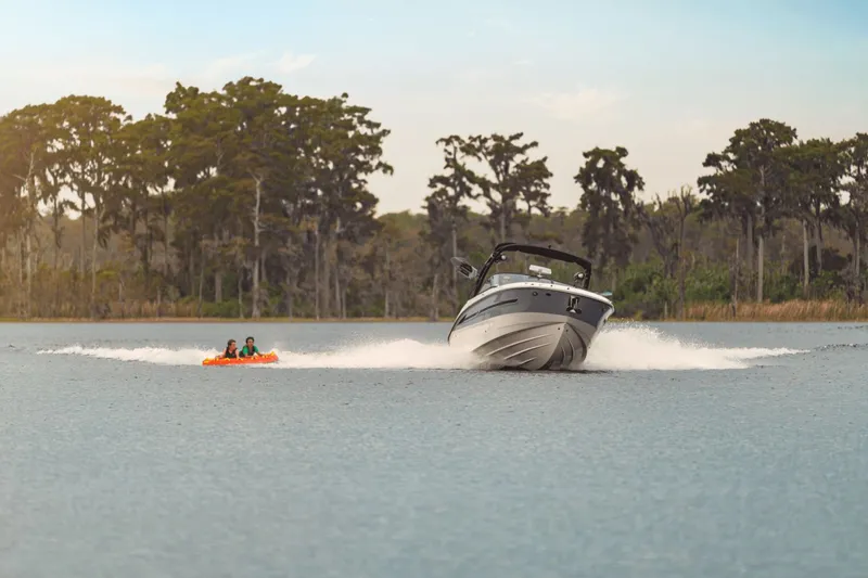 Slide: The Image of A 2025 Sea Ray SDX 270 Surf towing two people on an inflatable tube across a calm lake. - 22