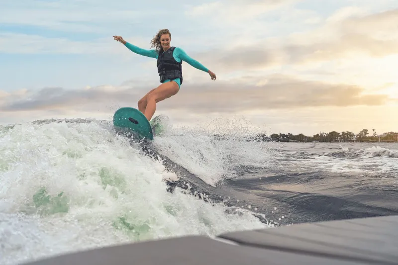 Slide: The Image of A woman surfs on a wave behind a boat at sunset. - 26