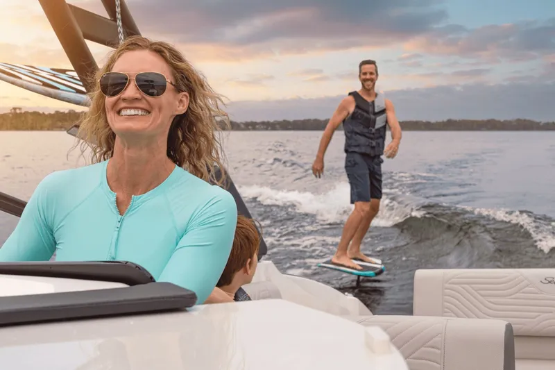 Slide: The Image of A woman steers a Sea Ray SDX 270 Surf boat as a man surfs behind. - 13