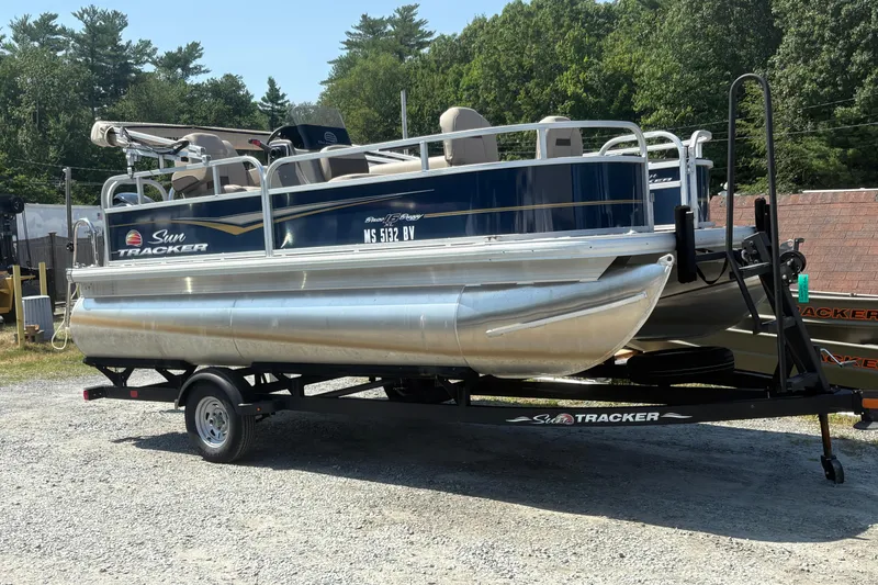 The Image of 2024 Sun Tracker Bass Buggy 16 DLX pontoon boat on trailer, parked outdoors. - 1