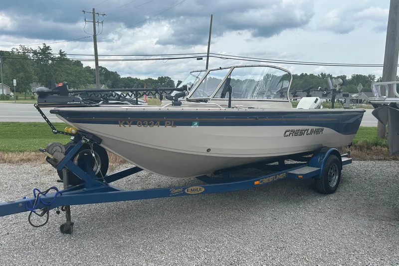 The Image of 2001 Crestliner 1850 O/B boat on trailer, parked outdoors under cloudy sky. - 0