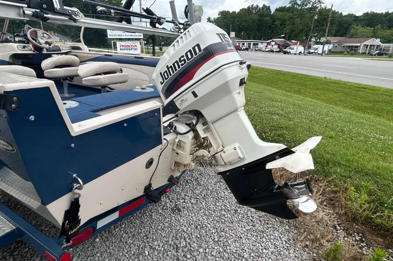 Slide: The Image of 2001 Crestliner 1850 O/B boat with Johnson outboard motor, parked on gravel near a road. - 2