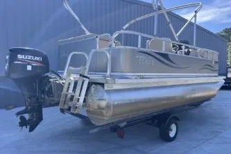 Slide: The Image of 2012 Avalon Tahoe pontoon boat with Suzuki outboard motor, parked on trailer. - 2