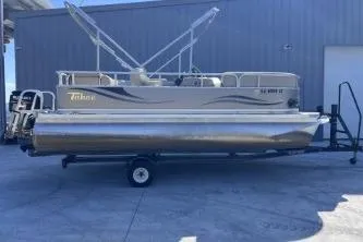 The Image of 2012 Avalon Tahoe pontoon boat on trailer, parked outdoors near a building. - 1