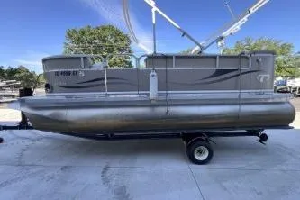 Slide: The Image of 2012 Avalon Tahoe pontoon boat on trailer, parked outdoors under clear blue sky. - 6