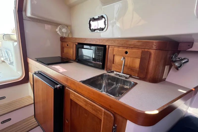 Slide: The Image of 2004 Hunt Yachts Surfhunter 29 interior galley with sink, microwave, and wooden cabinetry. - 21