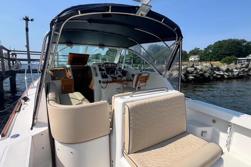 Slide: The Image of 2004 Hunt Yachts Surfhunter 29 interior with seating and helm, docked by rocky shoreline. - 9