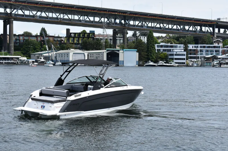 Slide: The Image of 2023 Cobalt R8 boat cruising on a river with a bridge and buildings in the background. - 2