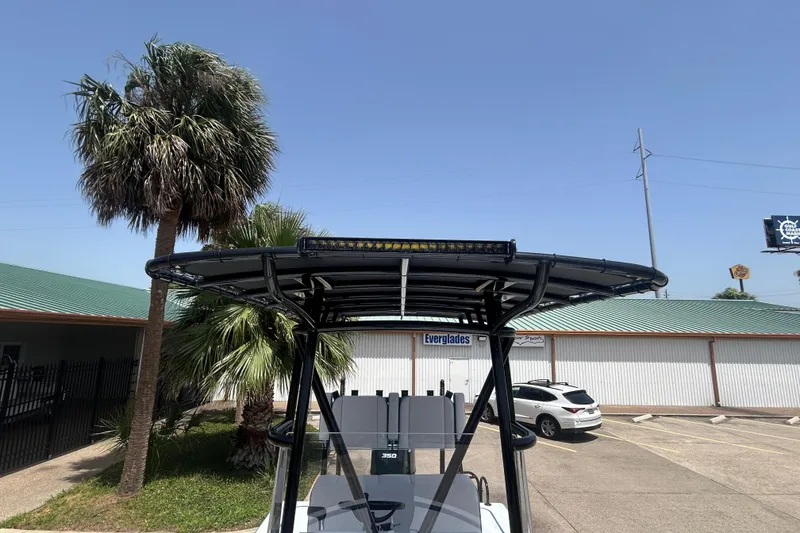 Slide: The Image of 2026 Shallow Sport 25 X3 boat with T-top, parked near palm trees and buildings. - 10