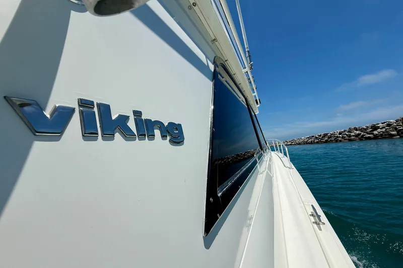 Slide: The Image of 1994 Viking 47 Convertible yacht cruising near rocky shoreline under clear blue sky. - 69