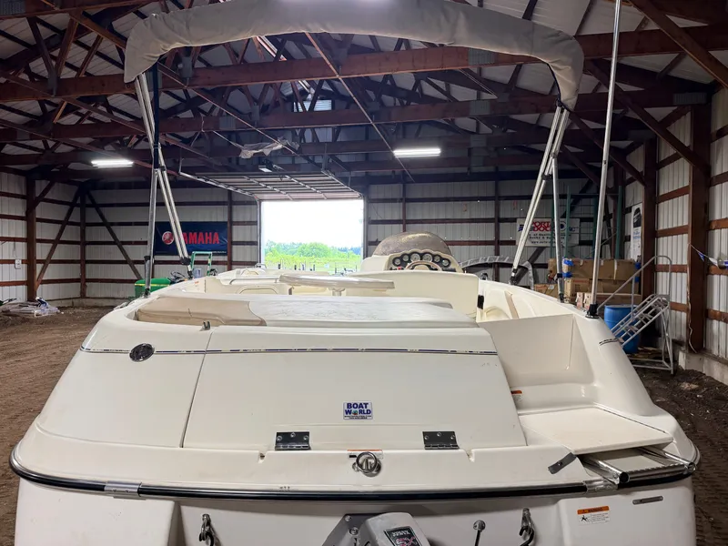 Slide: The Image of A 2003 Glastron DX215 deck boat in a storage facility, featuring a raised bimini top. - 38