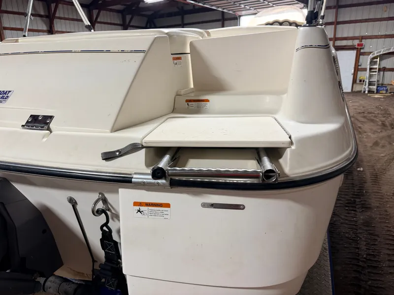Slide: The Image of Stern of a Glastron DX215 deck boat with swim platform and ladder in a storage facility. - 48