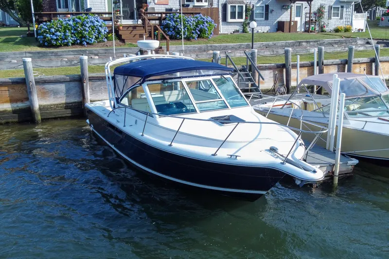 Slide: The Image of 2001 Tiara Yachts 2900 Coronet docked by waterfront homes, featuring blue canopy and sleek design. - 6