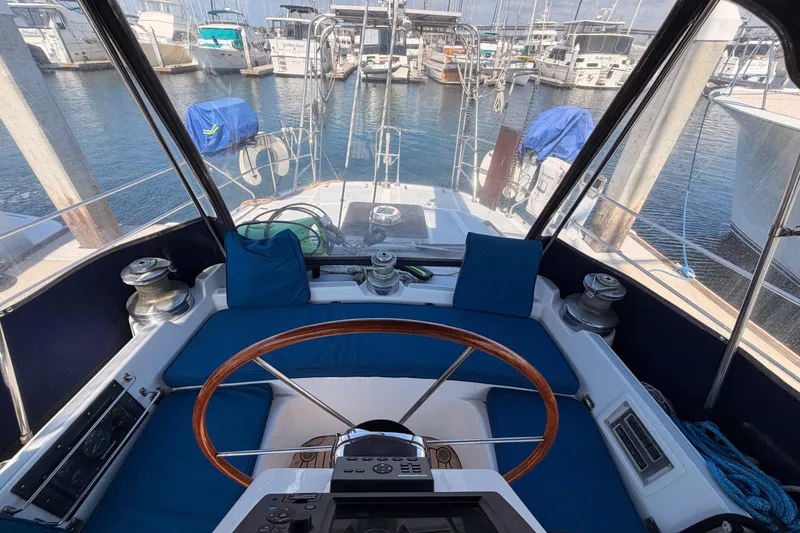 Slide: The Image of Cockpit view of a 1991 Hylas 51 sailboat, featuring a wooden steering wheel and marina backdrop. - 41