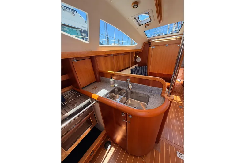Slide: The Image of Interior of 2007 Saga 409 sailboat featuring a compact wooden kitchen with sink and stove. - 70