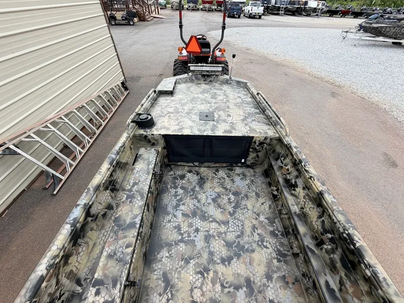 Slide: The Image of A rugged aluminum boat with camouflage pattern, sitting on a trailer next to a building. - 6