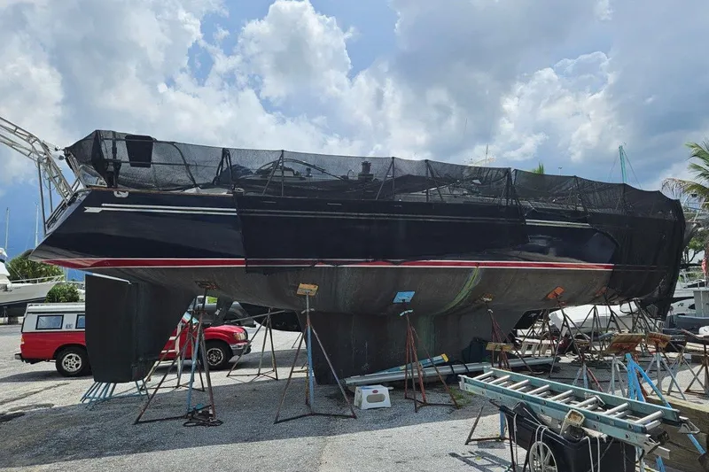 The Image of 1987 Tayana 52 sailboat on dry dock, surrounded by maintenance equipment under a cloudy sky. - 0