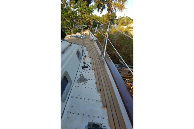 Slide: The Image of Deck view of 1987 Tayana 52 sailboat with wooden railings and lush greenery. - 8