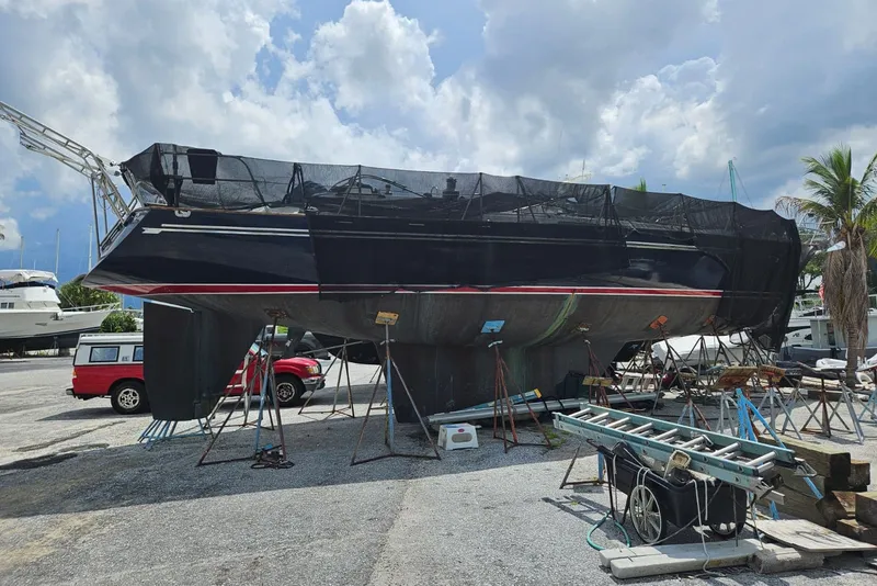 Slide: The Image of 1987 Tayana 52 sailboat on dry dock, surrounded by maintenance equipment under a cloudy sky. - 31