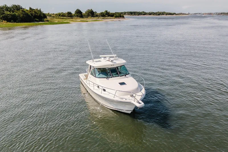 Slide: The Image of 2013 Pursuit OS 345 Offshore boat cruising on calm waters near a lush shoreline. - 2