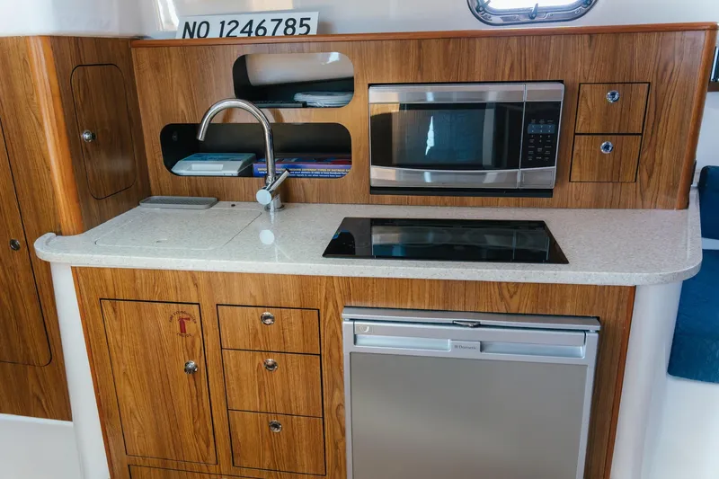 Slide: The Image of 2013 Pursuit OS 345 Offshore boat kitchen with wood cabinetry, sink, microwave, and stove. - 7