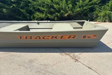 The Image of 2026 Tracker Grizzly 12 Jon boat on concrete, surrounded by greenery. - 0