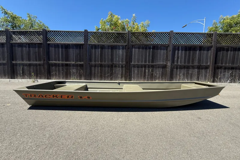 The Image of 2026 Tracker Grizzly 14 Jon boat on pavement, wooden fence background, clear sky. - 0