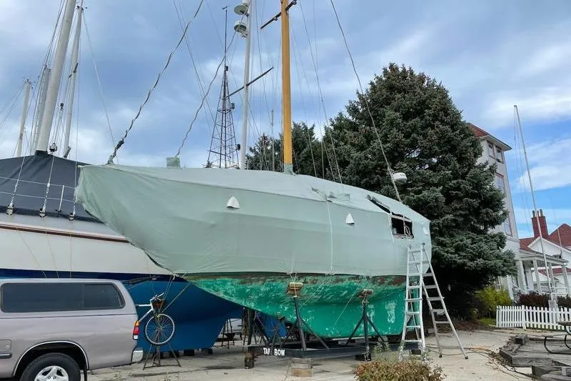 Slide: The Image of 1980 Ta Shing Baba 30 sailboat on land, covered, with ladder and trees nearby. - 1