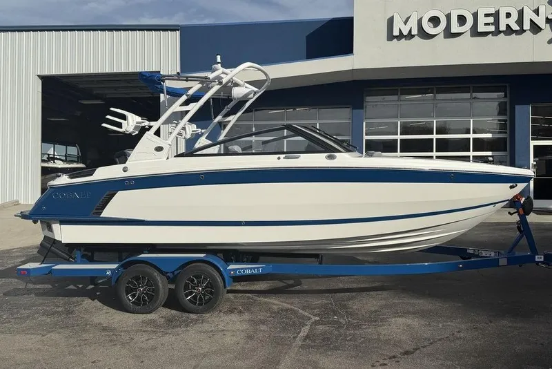 The Image of 2026 Cobalt R4 Surf boat on trailer outside a modern showroom. - 1