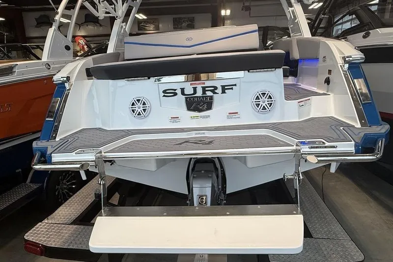 Slide: The Image of 2026 Cobalt R4 Surf boat rear view in showroom, featuring swim platform and speakers. - 10