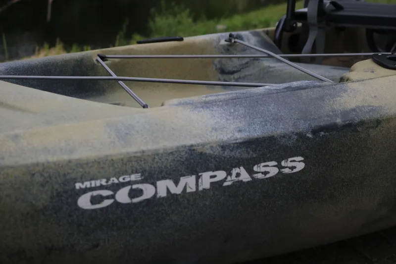 Slide: The Image of 2023 Hobie Mirage Compass kayak with camouflage design near a serene water body. - 6