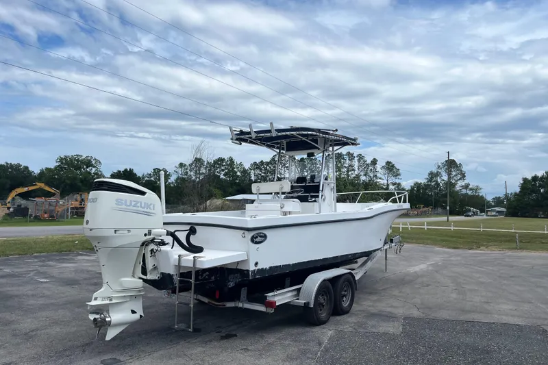 Slide: The Image of White Duskey 256 boat on trailer with Suzuki outboard motor, parked outdoors under cloudy sky. - 2