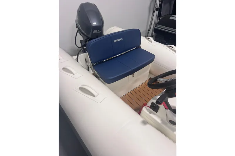 Slide: The Image of 2026 Brig Falcon 360 inflatable boat with blue seating and 25 HP outboard motor. - 2