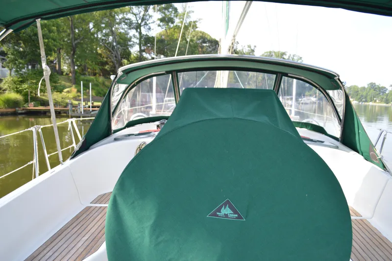 Slide: The Image of 1999 Beneteau 411 sailboat cockpit with green canvas cover, docked near lush greenery. - 10