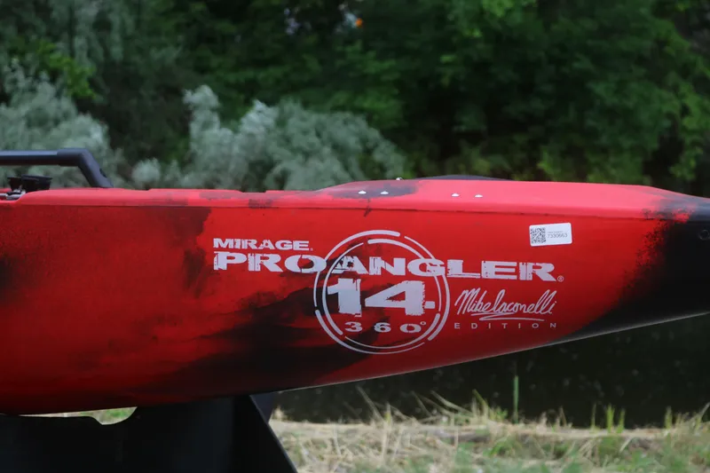 Slide: The Image of Red 2023 Hobie Mirage Pro Angler 14 kayak, Mike Iaconelli edition, near lush greenery. - 2