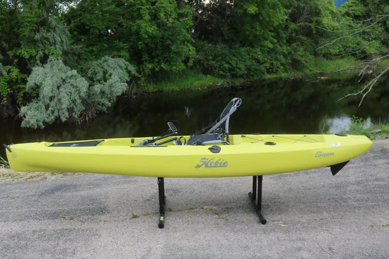 The Image of 2025 Hobie Mirage Compass kayak in vibrant yellow, displayed outdoors near a serene waterway. - 0