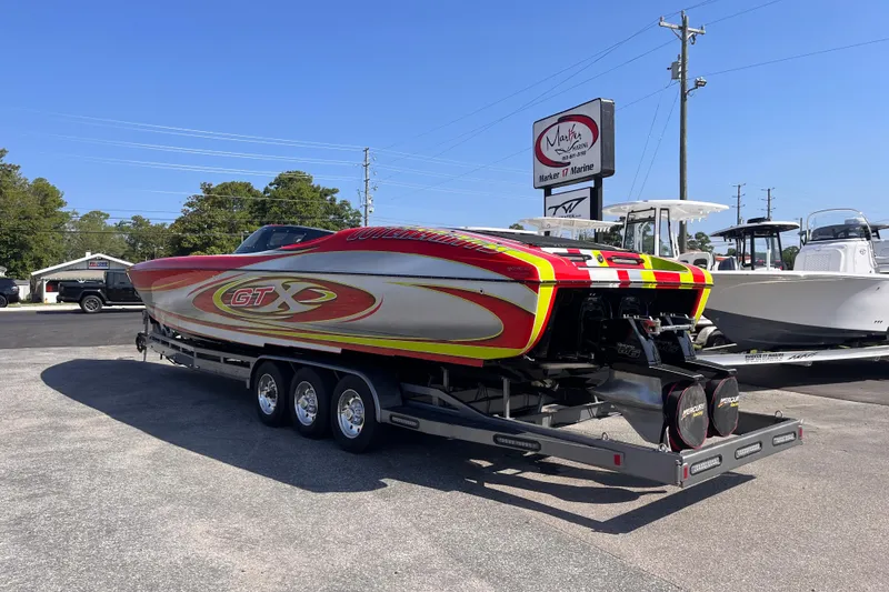 Slide: The Image of 2007 Outerlimits 39 GTX powerboat on trailer, vibrant red and yellow design, parked at marina. - 3