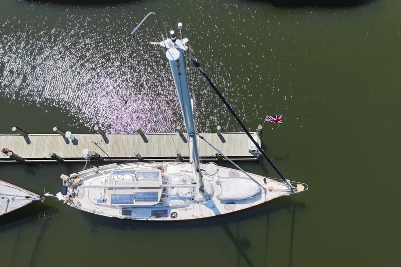 Slide: The Image of Aerial view of 1989 Mason 54 sailboat docked, with British flag and sparkling water. - 64