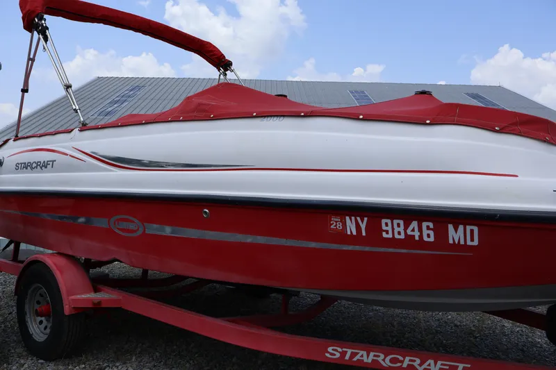 Slide: The Image of 2008 Starcraft 2000 IO Limited boat with red cover on trailer, parked outdoors. - 10