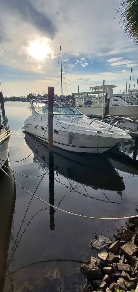 The Image of A 2002 Wellcraft 3300 Martinique docked in a marina, surrounded by calm water and other boats. - 0
