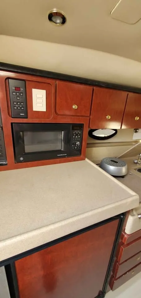 Slide: The Image of The 2002 Wellcraft 3300 Martinique's galley features a microwave and wooden cabinets. - 11