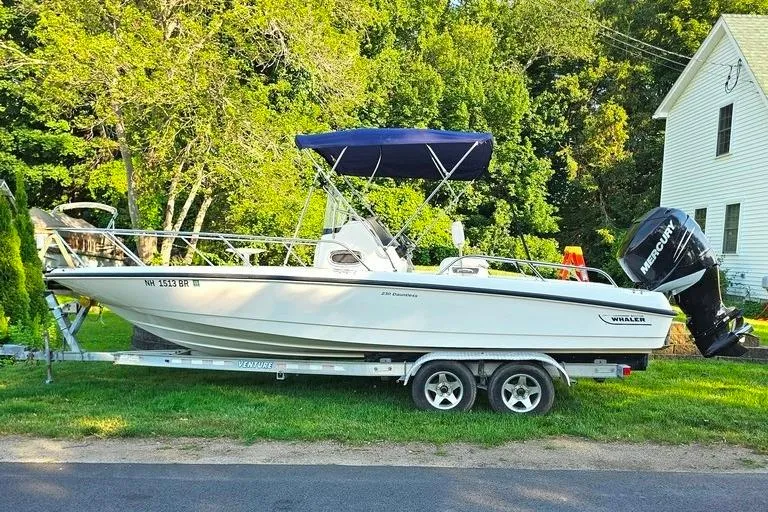 The Image of 2011 Boston Whaler 230 Dauntless boat on trailer, parked near a house with lush greenery. - 0