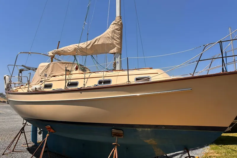 The Image of 1991 Island Packet 29 sailboat on stands, beige hull, blue bottom, clear sky background. - 0
