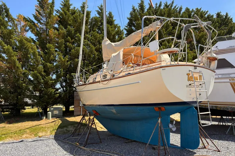 Slide: The Image of 1991 Island Packet 29 sailboat on stands, surrounded by trees and parked vehicles. - 2