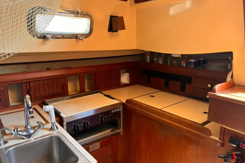 Slide: The Image of Cozy 1991 Island Packet 29 yacht galley with wooden cabinetry and compact kitchen amenities. - 20